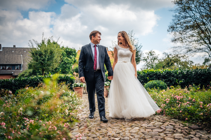 Brautpaarshooting händehaltend auf Kamera zugehen und lachen