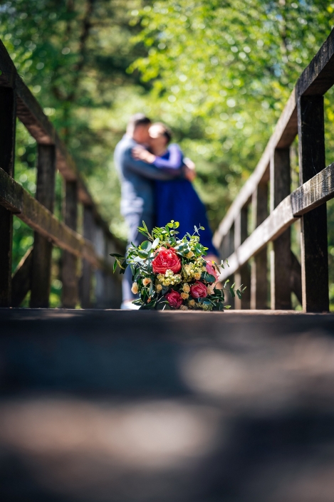Brautstrauß liegt auf der Brücke und das Brautpaar küsst sich im Hintergrund