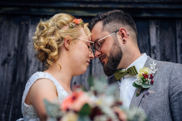 Brautpaarshooting mit unscharfen Blumenstrauß im Vordergrund und dunklem Holzhintergrund