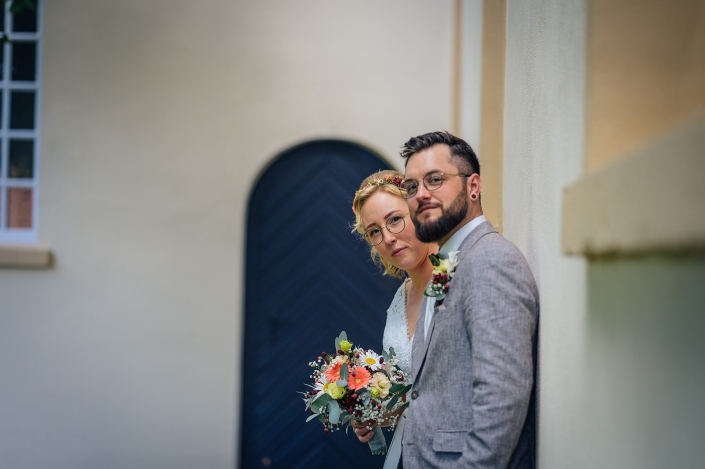 Brautpaarshooting Brautpaar lehnt sich an heller Wand vor der Kirche an